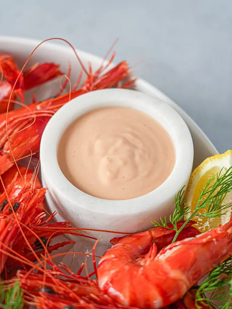 Close-up Bowl of Cocktail Sauce placed on a tray surrounded by fresh prawns, perfect for serving.