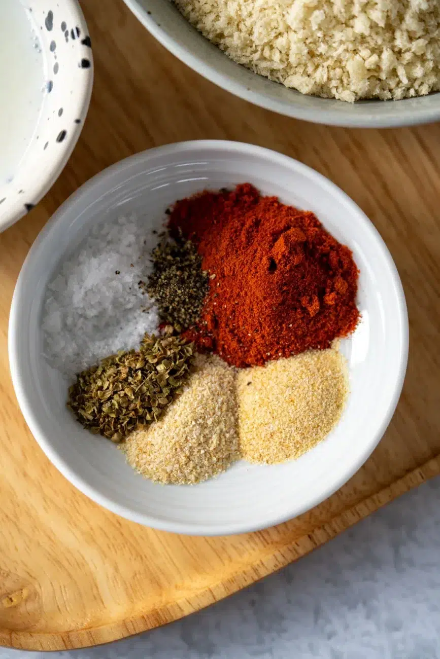 Close-up of assorted spices in a white bowl for seasoning crispy baked chicken tenders.