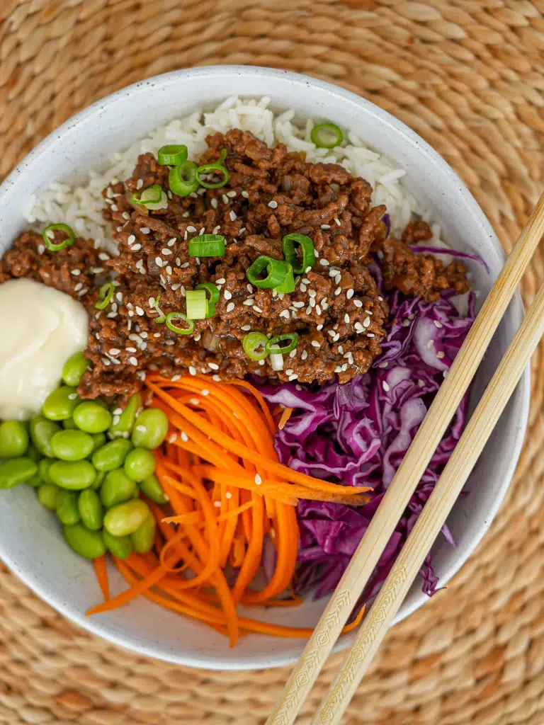 a bowl of tender beef slices and vegetables in teriyaki sauce, with a garnish of green onions and sesame seeds
