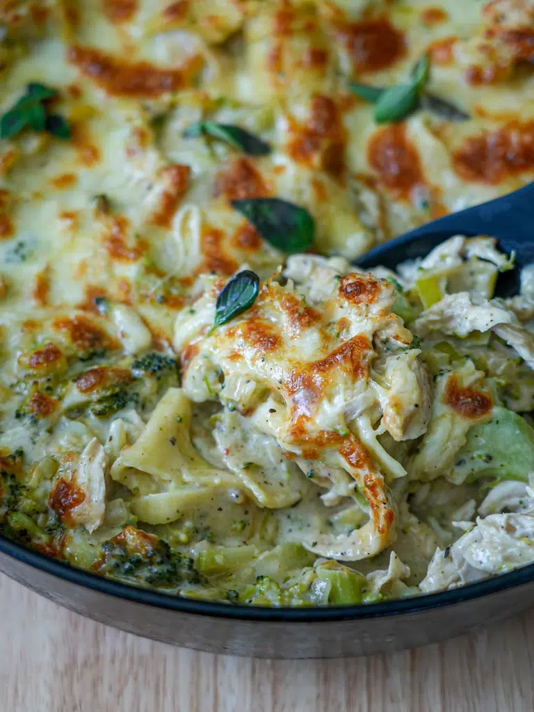 Close-up of a spoon lifting a slice of creamy white lasagna from a pan