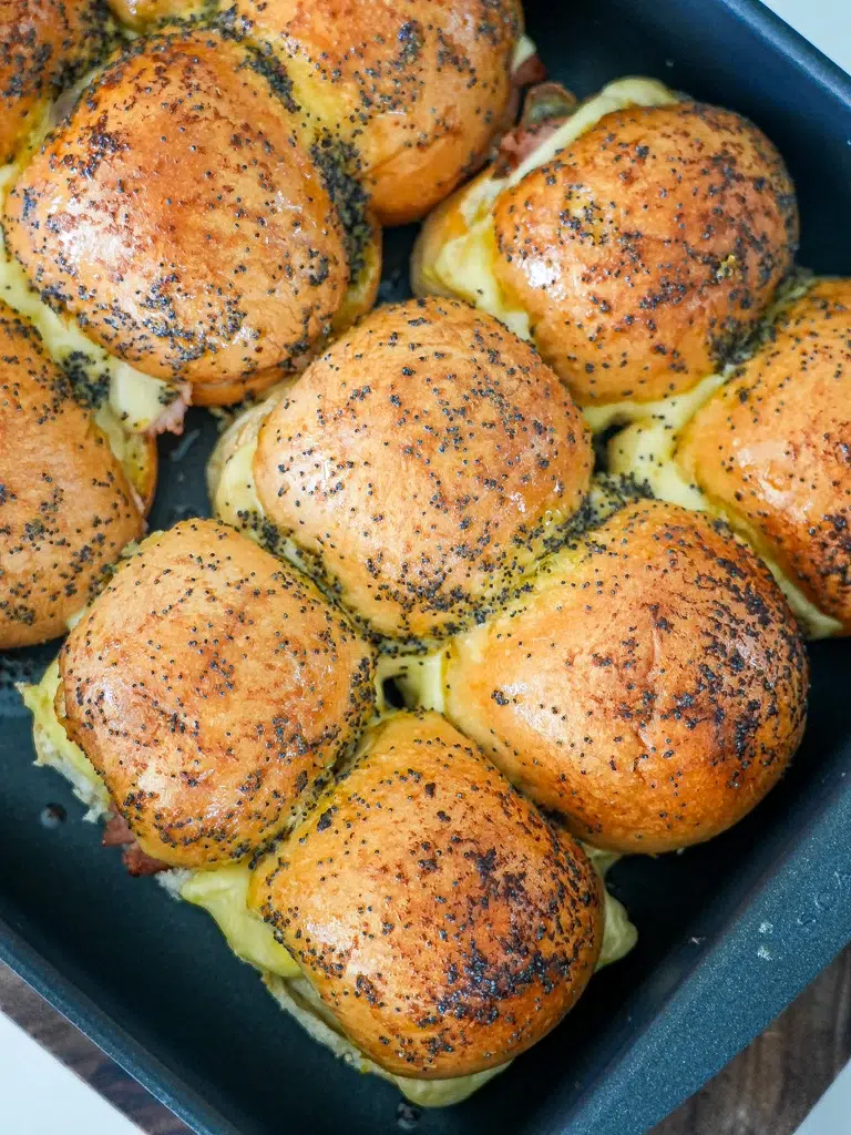 Overhead view of baked ham and cheese sliders in a pan, topped with melty yellow cheese and arranged closely together.