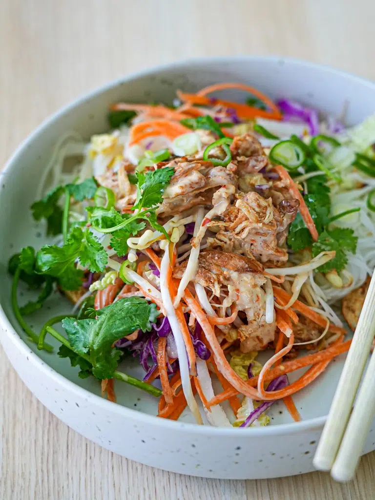Bang Bang Chicken Salad served in a bowl with chopsticks resting on the rim.