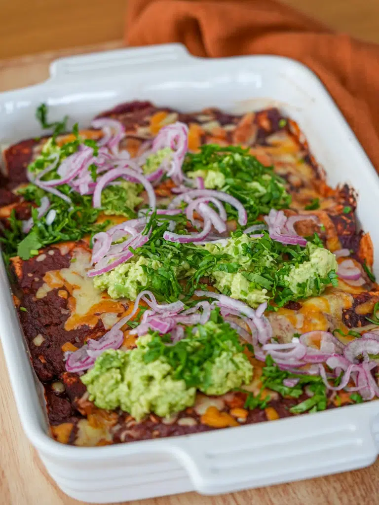 Delicious cheesy chicken enchiladas topped with creamy avocado, onion, and fresh herbs.