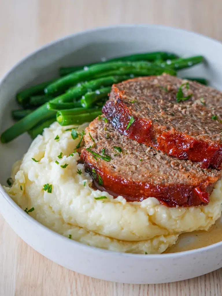 Tangy tomato-glazed meatloaf served with creamy mashed potatoes and green beans.