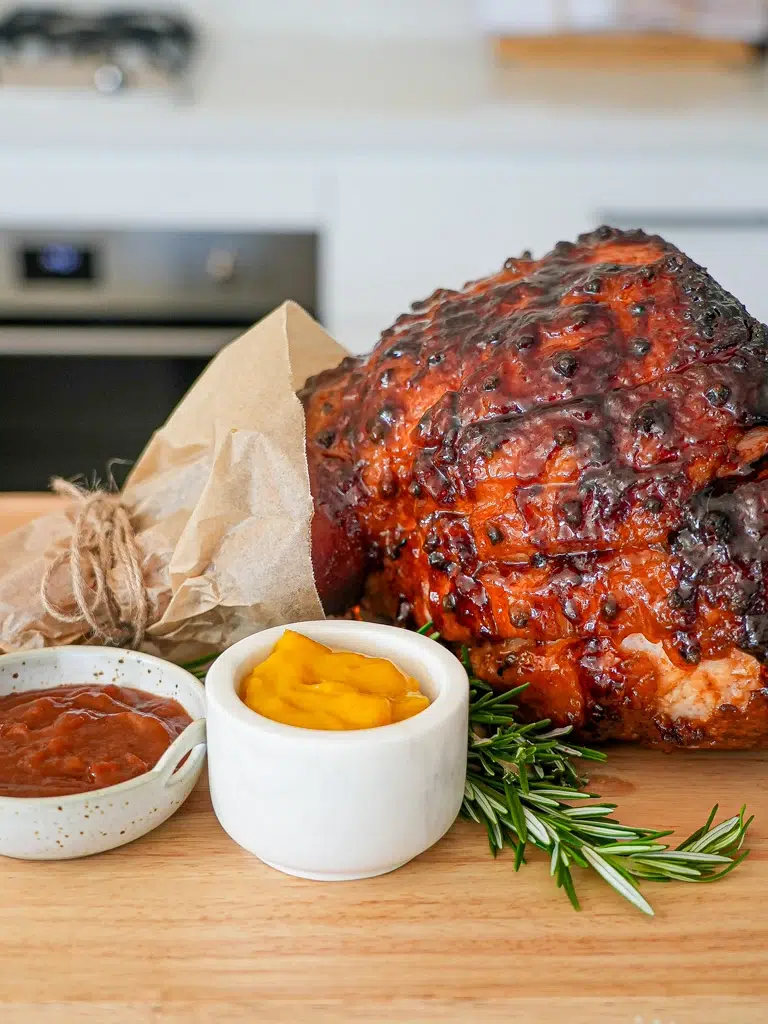 Whole glazed ham on a wooden board, uncarved, with a shiny, caramelized glaze in a long shot view.