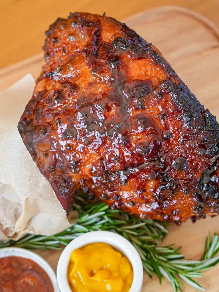 Close-up of a whole glazed ham on a wooden board, highlighting the caramelized glaze and rich texture.