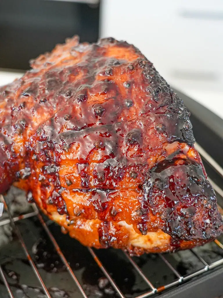Glazed ham resting on a rack in a roasting pan, ready for serving.