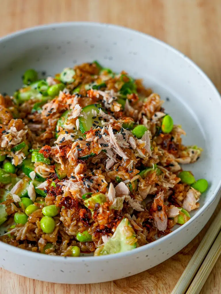 Close-up of a bowl filled with rice, tuna, and avocado, with chopsticks placed beside the bowl.