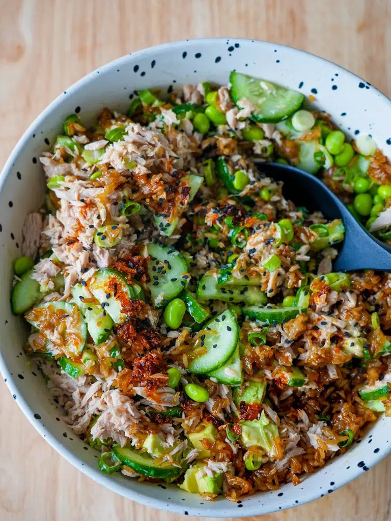 Overhead view of a bowl of rice with a spoon, topped with tuna and avocado.