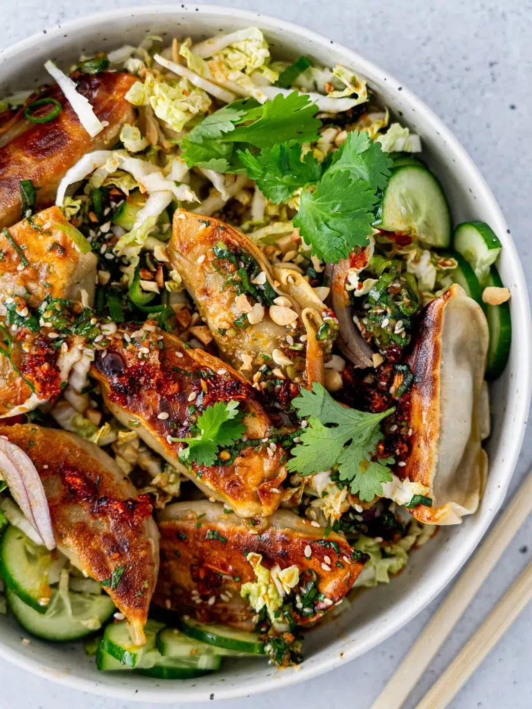 A colorful dumpling salad with fresh vegetables and steamed dumplings arranged on a white plate.