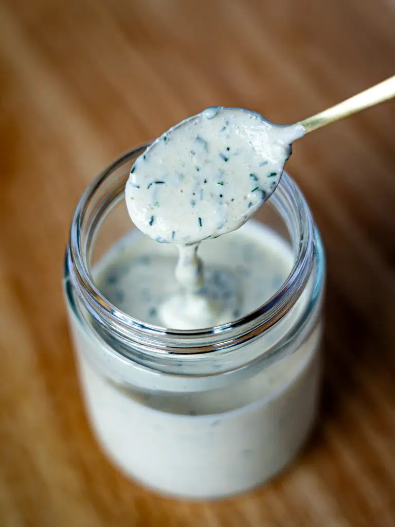 Spoon dripping homemade ranch dipping sauce into a glass jar.