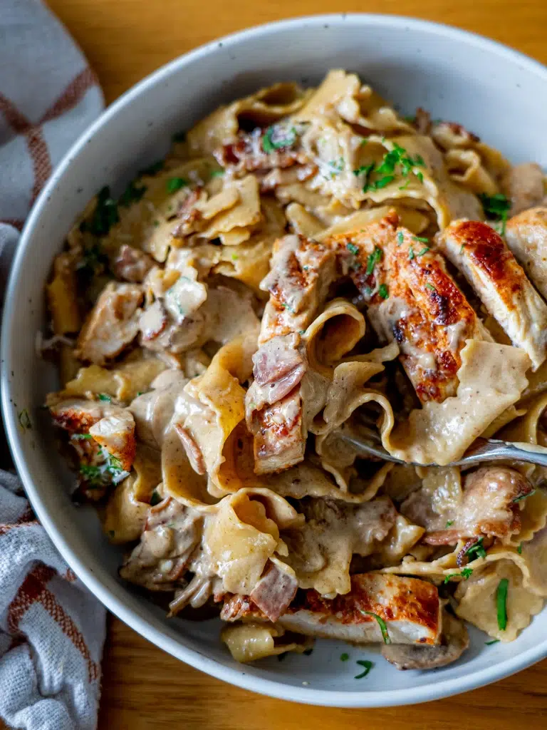 Top view of Chicken Boscaiola Pasta plated with a fork digging in, featuring a creamy sauce, bacon, and mushrooms.