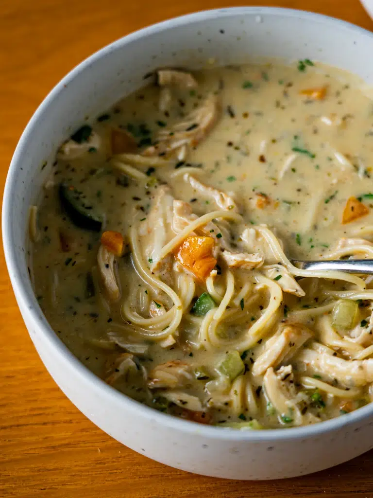 Close-up of creamy lemon chicken noodle soup plated with a spoon.