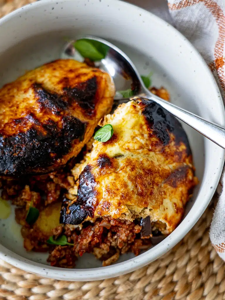 A comforting bowl of homemade moussaka with a spoon, topped with fresh herbs.