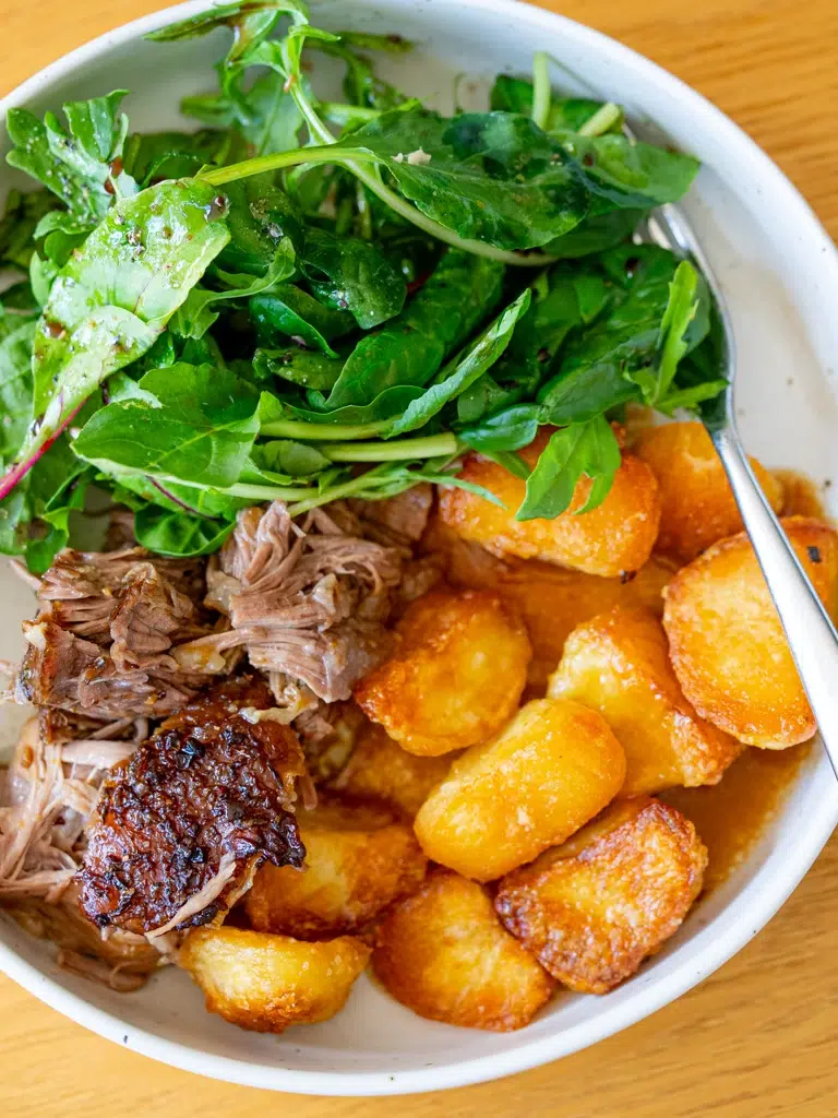 Top view of Rosemary Garlic Lamb Shoulder with gravy served on a white plate with a fork on the side.