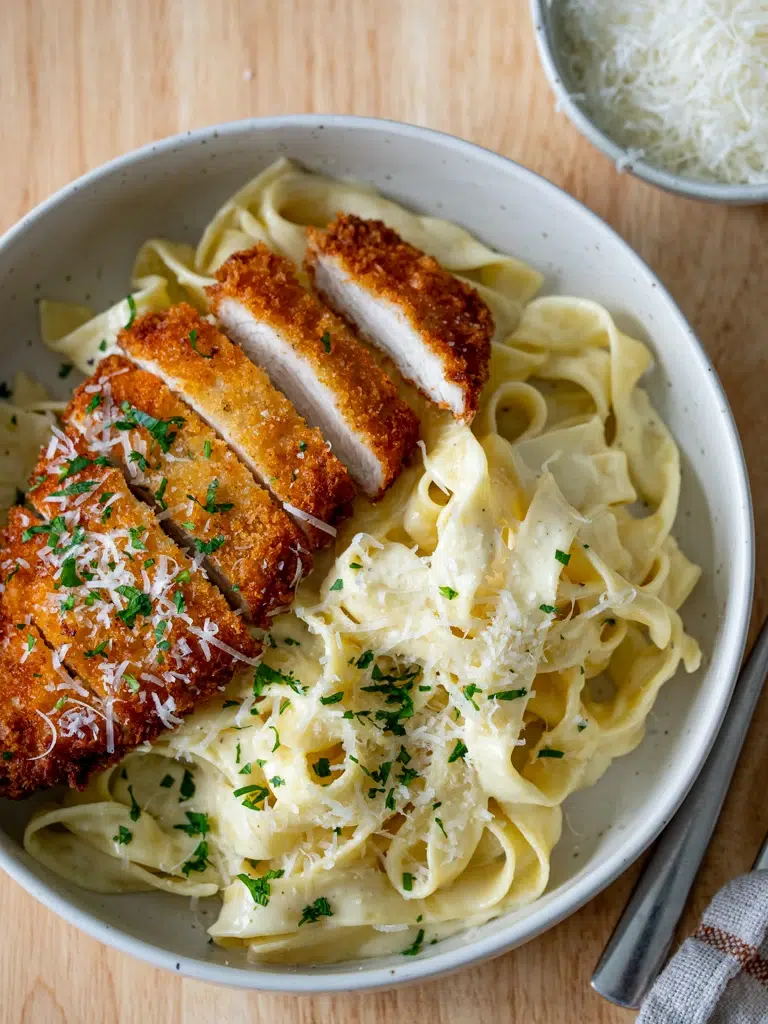 Top view of crispy chicken fettuccine Alfredo plated with a creamy sauce and garnish.