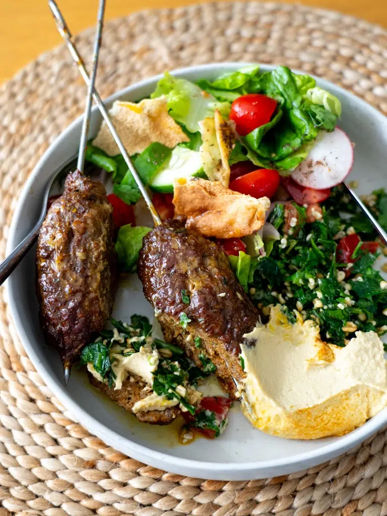 Plated lamb kofta alongside vibrant fattoush salad and creamy hummus.