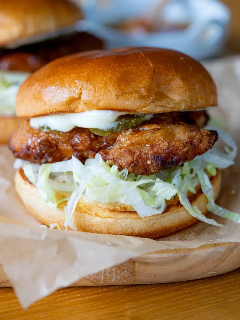 Close-up of a hot honey crunch chicken burger with crispy fried chicken, shredded lettuce, pickles, and mayonnaise in a soft brioche bun.