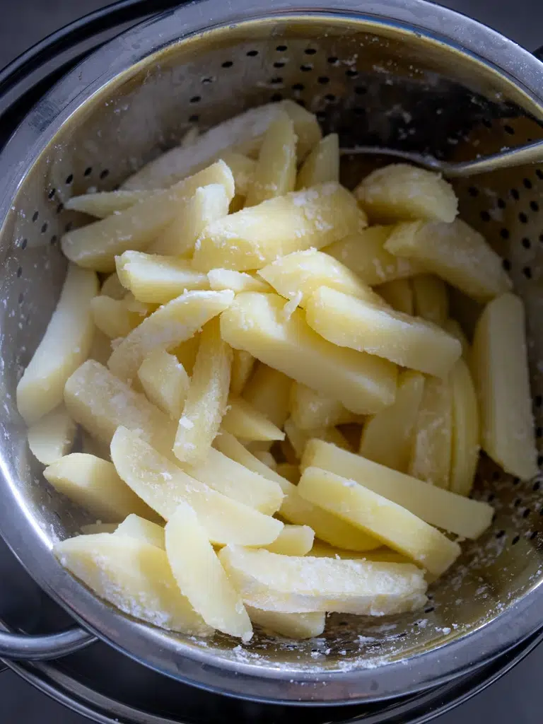 Parboiled potato chips in a colander, ready for baking into crispy oven fries.