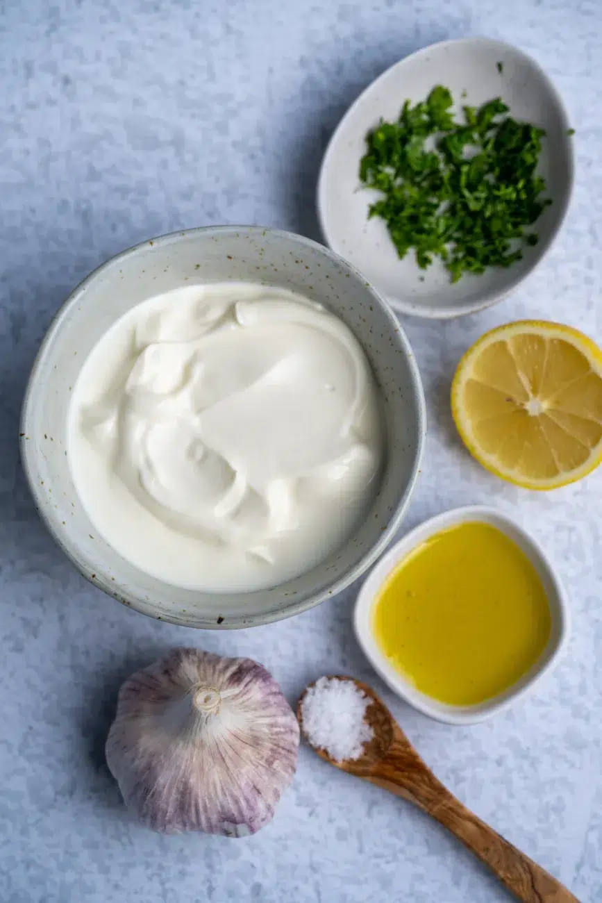 Flat lay of ingredients for garlic yoghurt sauce: Greek yoghurt, fresh garlic, lemon, and salt