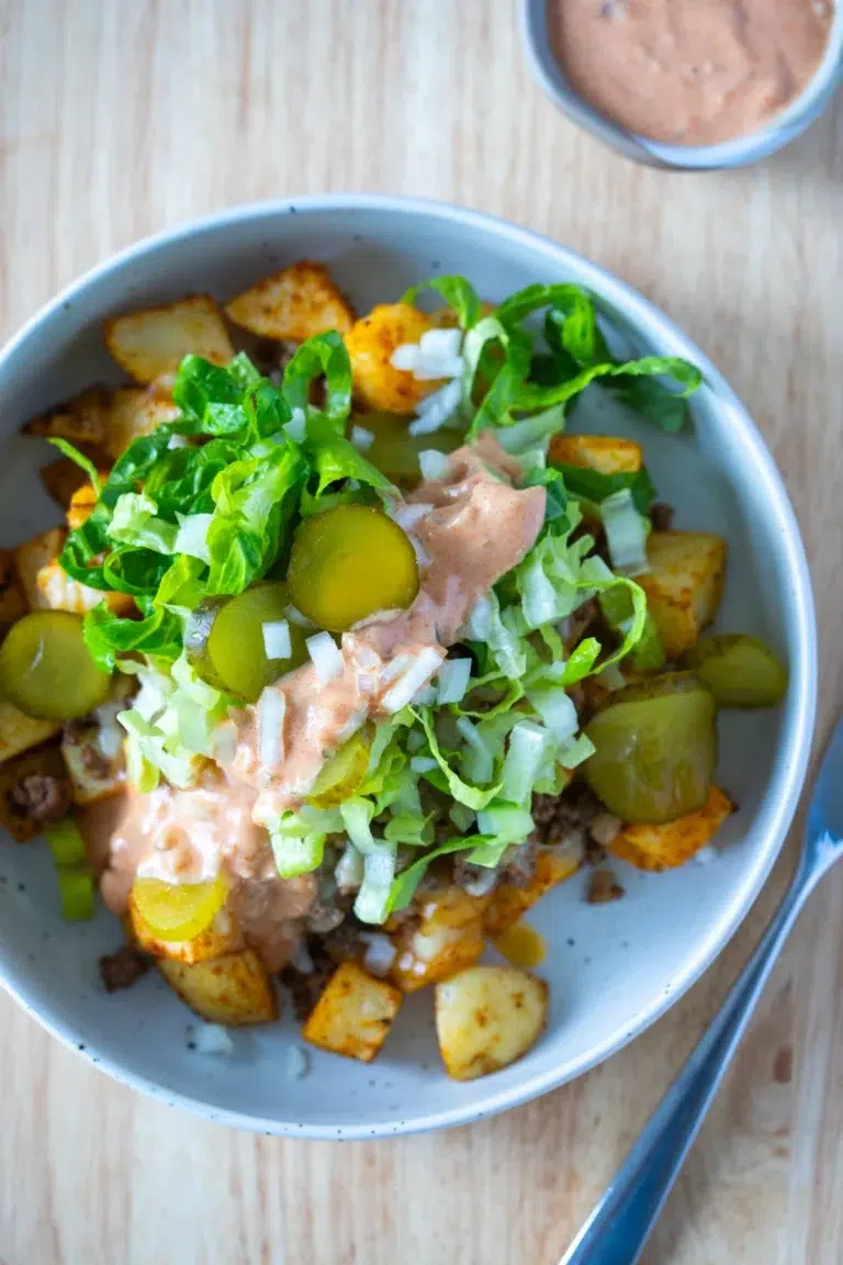 Top view of a Loaded Potato Big Mac Bowl with crispy potatoes, seasoned beef, shredded lettuce, pickles, diced onions, and special sauce, served in a speckled ceramic bowl.