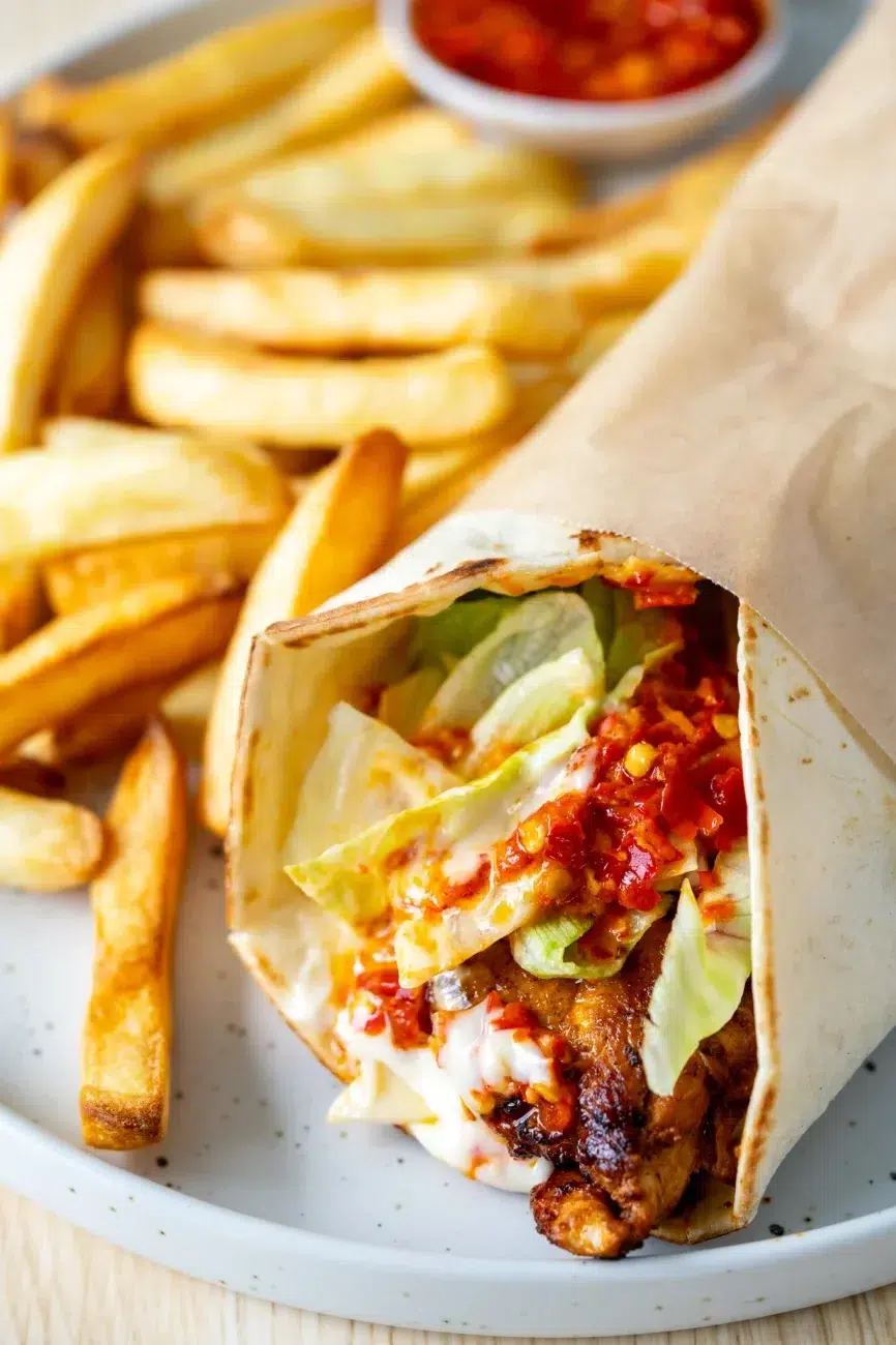 Close-up of Portuguese-style chili chicken wrap with lettuce, sauce, and fries on a plate