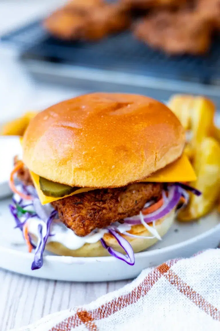 Crispy fried chicken burger with ranch slaw, cheese and pickles on a toasted brioche bun, served with crispy potato wedges