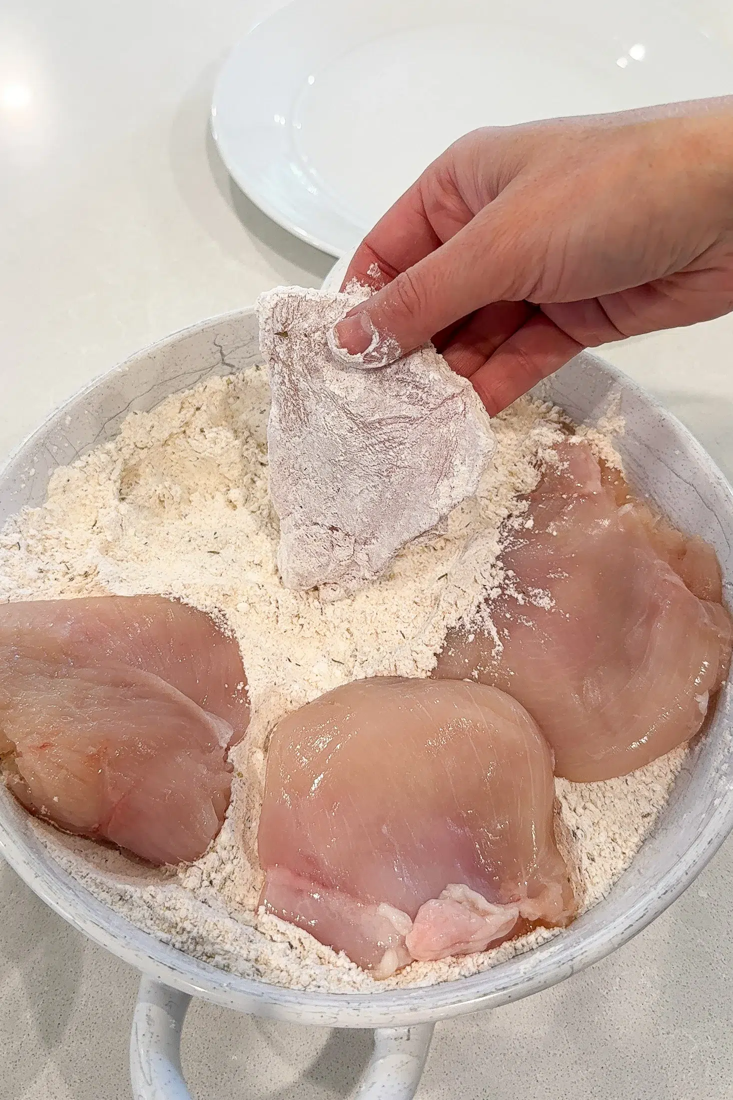 Chicken piece being dusted in seasoned flour coating