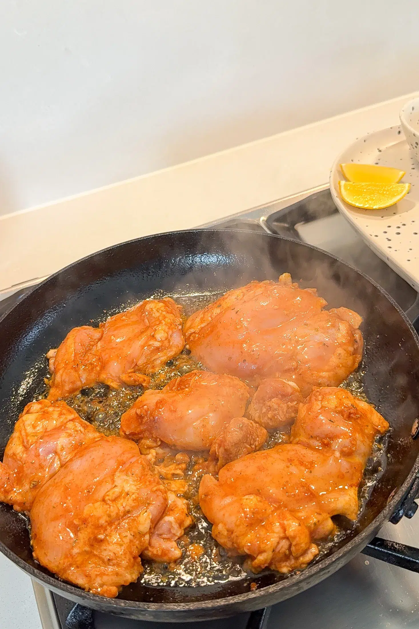 Marinated chicken thighs searing in a cast iron skillet on the stovetop with steam rising