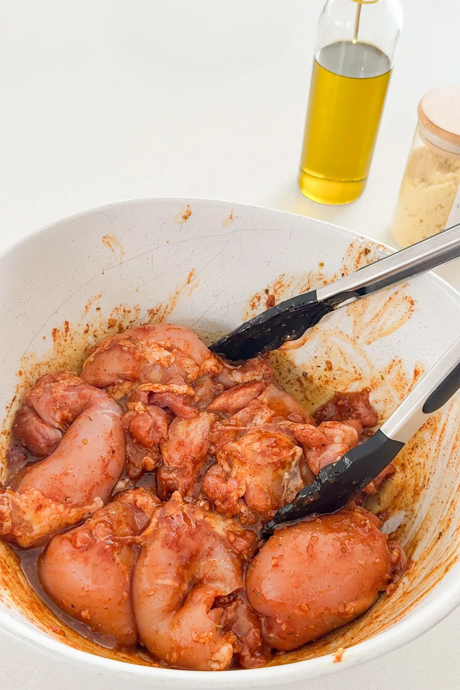 Raw chicken thigh fillets tossed in the garlic lemon marinade in a large white bowl with tongs