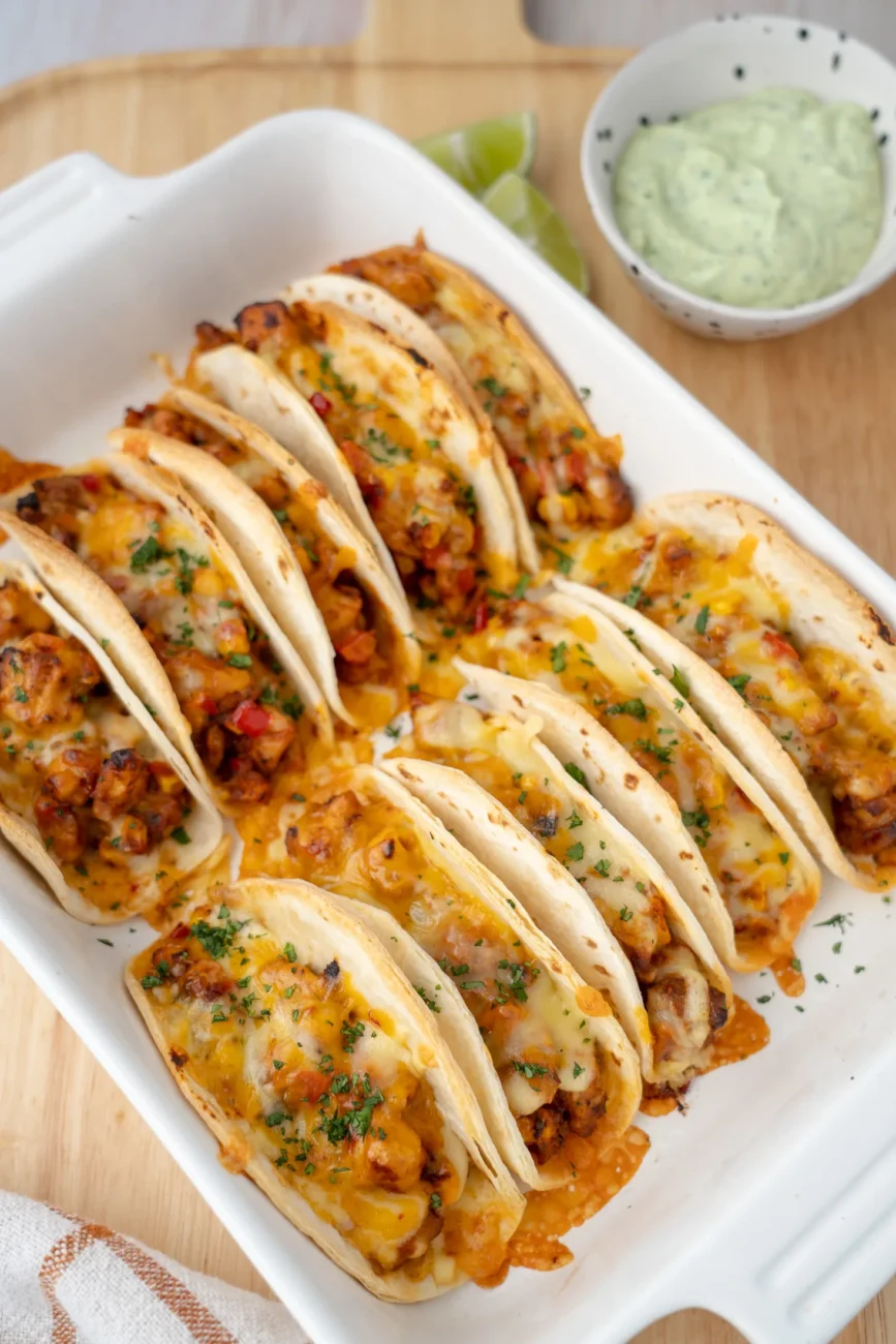 Baked Chicken Tacos in tray with avocado cream and lime wedges