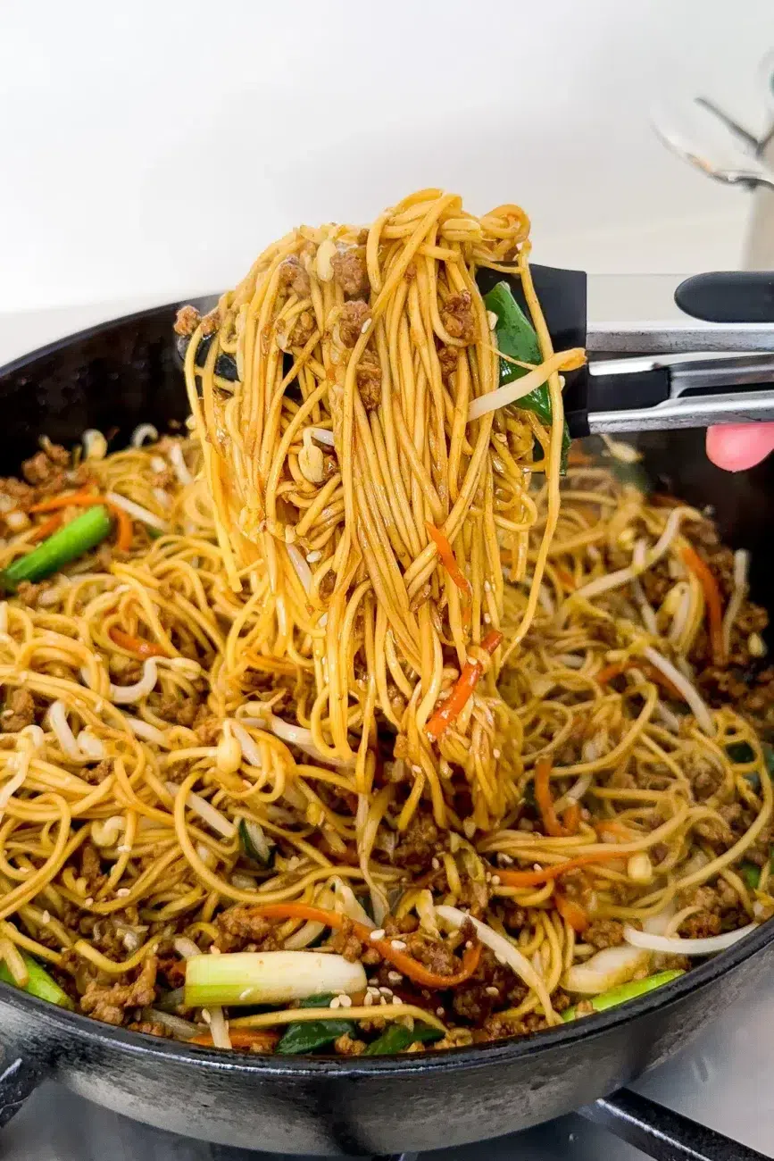 Tossed stir fry tongs pulling out noodles showing glossy sauce